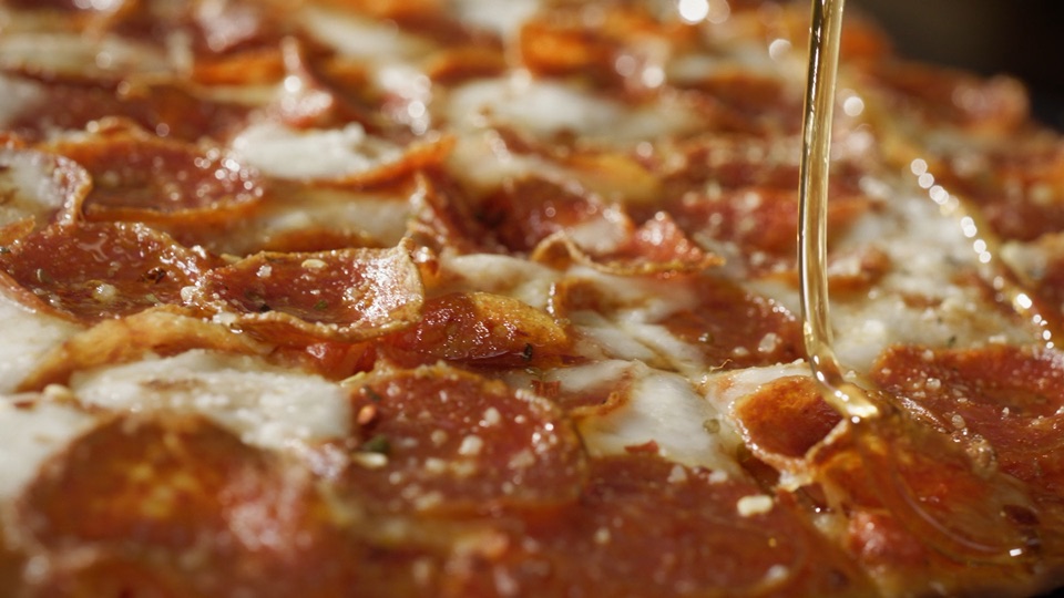 Honey poured over pizza in the finished Donatos Hot Honey commercial