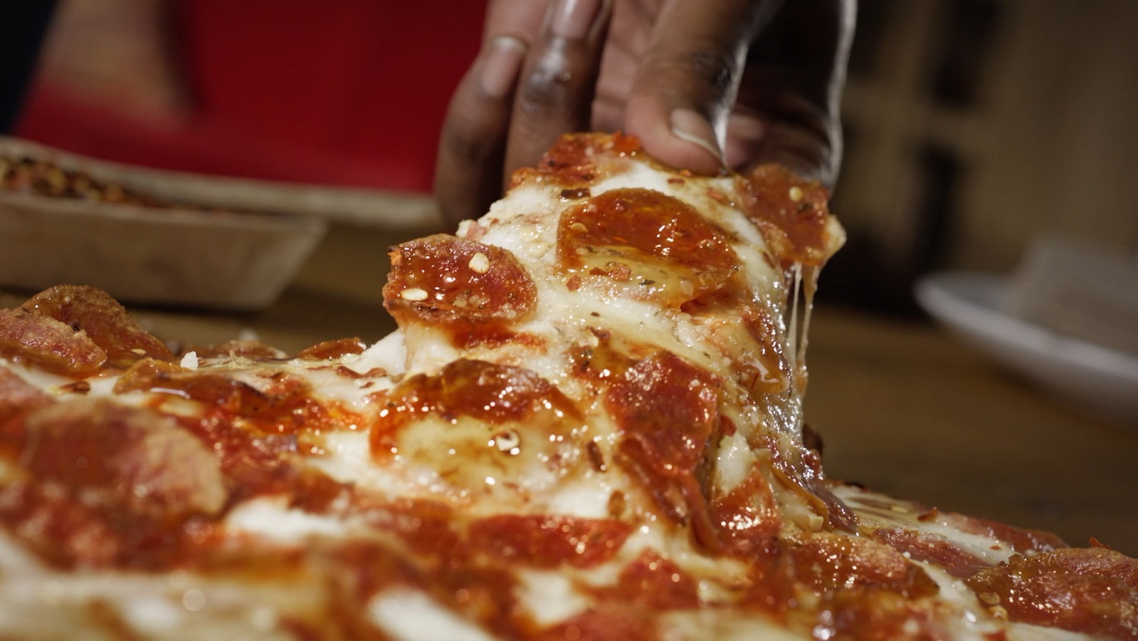 A hand lifting a pizza slice in the Donatos Hot Honey commercial